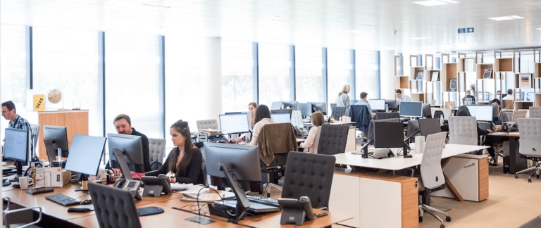 Busy open-plan office with staff working at desks with multiple monitors and desk phones