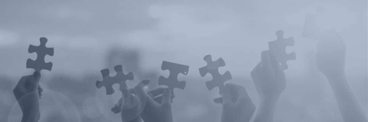 Hands holding up jigsaw puzzle pieces against the sky in a blue-tinted banner