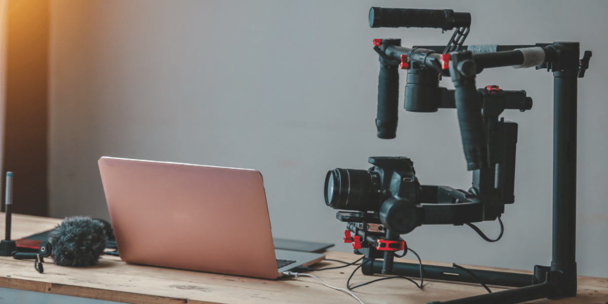 A desk with an open pink laptop, with a camera attached to a camera rig