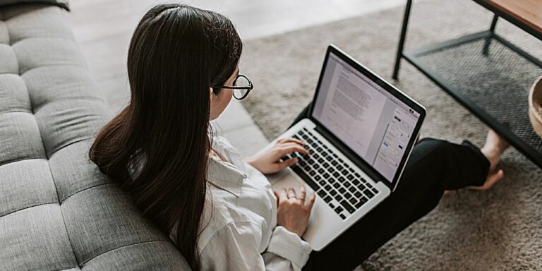 A woman sitting on her living room floor, typing on her laptop