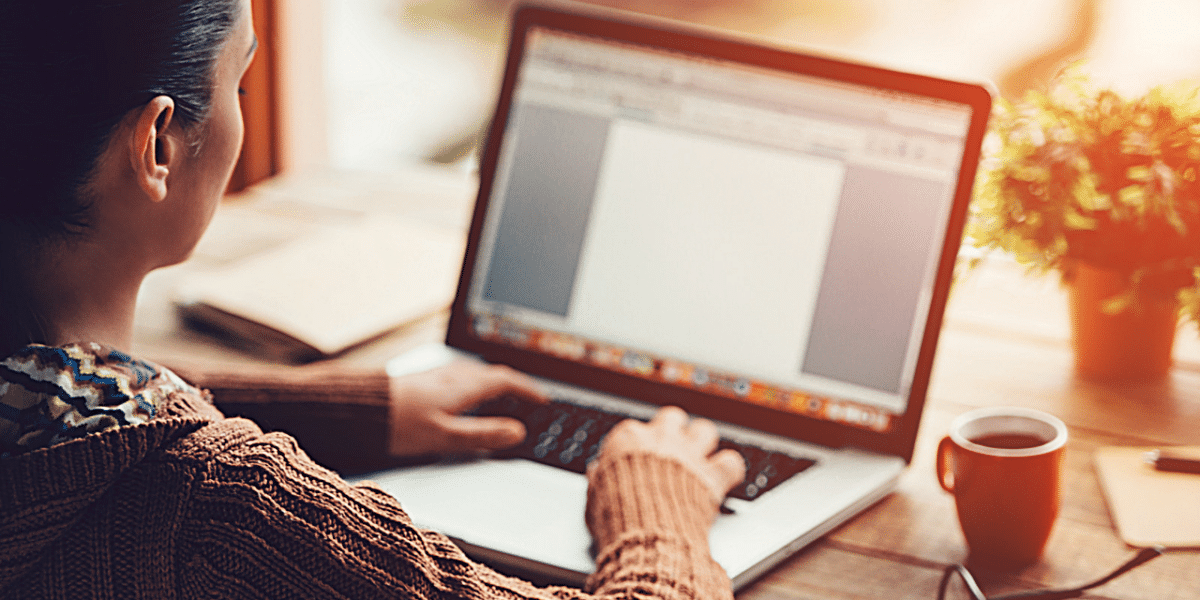 A woman at a desk with a plant on it, typing on her laptop