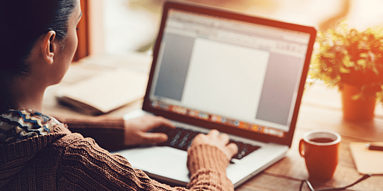 A woman at a desk with a plant on it, typing on her laptop